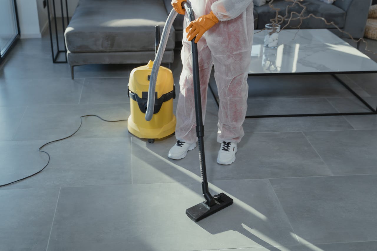 gallery-2 A professional cleaner in protective gear vacuuming the floor in a modern living room.