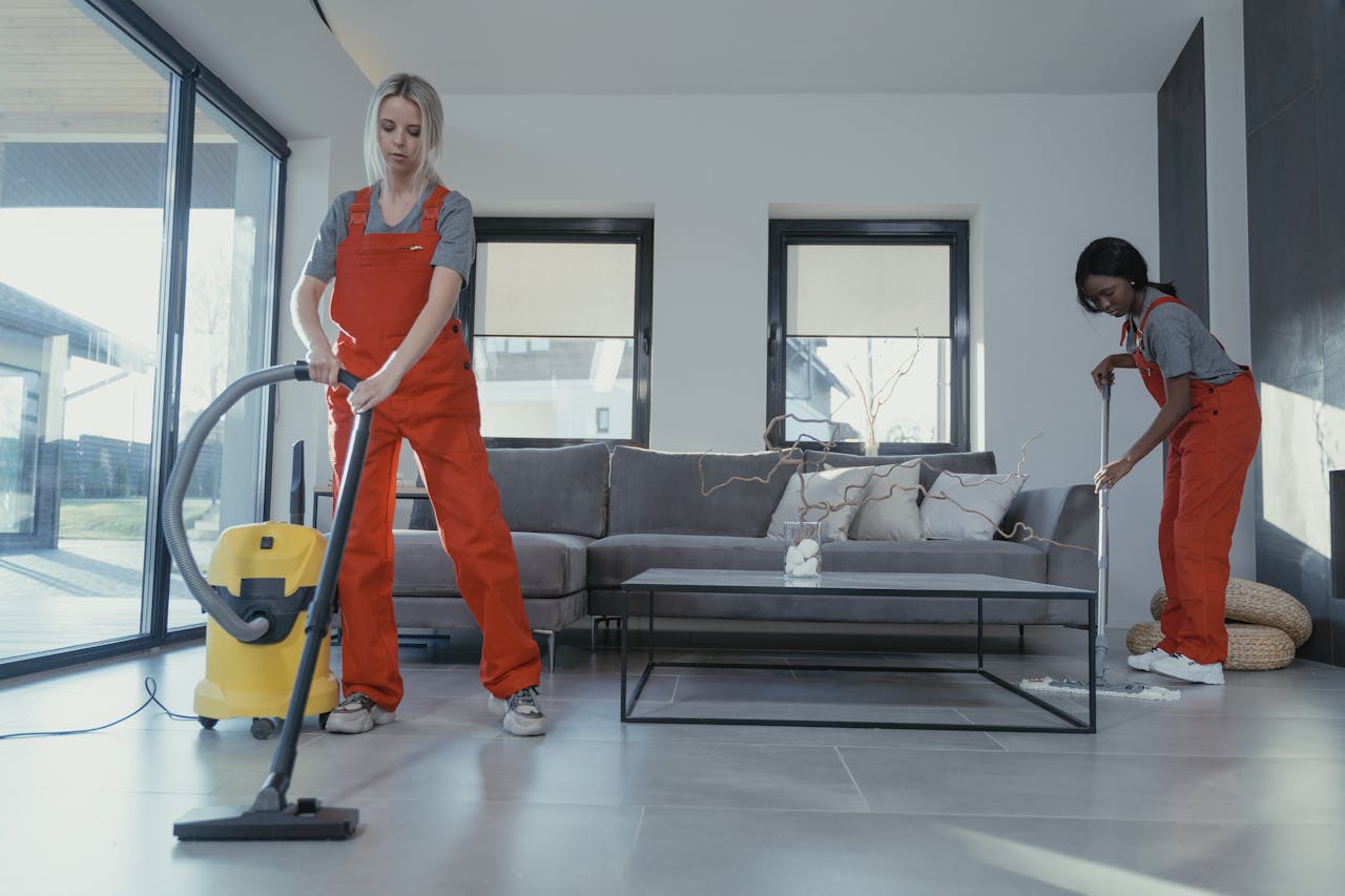 gallery-5 Two women in red overalls vacuuming and sweeping a modern living room.